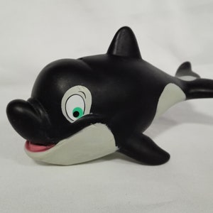Peut inclure: Jouet d'orque en caoutchouc noir et blanc avec un œil vert et un ventre blanc. L'orque est en position de nage avec la bouche ouverte.