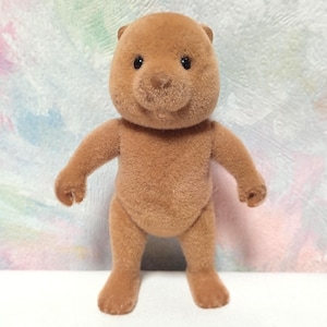 Peut inclure: Un ours en peluche brun avec une surface texturée. L'ours a de petits yeux noirs, un museau arrondi et des bras et des jambes tendus. Le jouet est debout contre un fond coloré et abstrait.