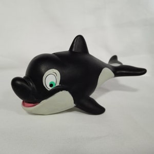 K&ouml;nnte beinhalten: Schwarz-wei&szlig;es Spielzeug-Orca aus Gummi mit einem gr&uuml;nen Auge und einem wei&szlig;en Bauch. Der Orca ist in Schwimmposition mit offenem Maul.