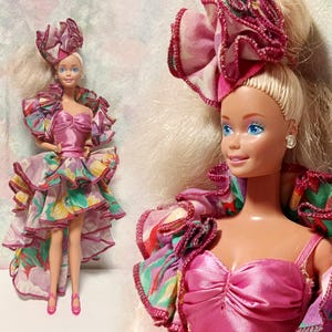 Puede incluir: Una muñeca con cabello rubio peinado en una coleta alta con un accesorio floral de tela. La muñeca viste un corpiño rosa sin tirantes y una falda asimétrica con un patrón floral multicolor, bordes con volantes y zapatos de color rosa.