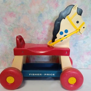 Op de afbeelding: Een vintage Fisher-Price paardenspeelgoed om op te rijden met een rode zitting, een blauwe opbergdoos en gele wielen. Het paard heeft een zwarte manen en staart en blauwe vlekken op zijn zij.