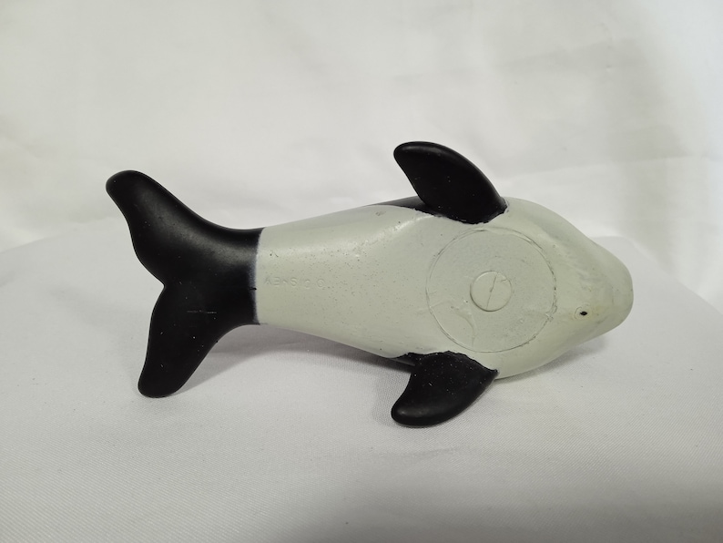 K&ouml;nnte beinhalten: Ein schwarzes und wei&szlig;es Plastikspielzeug-Orca-Wal. Der Wal liegt auf der Seite mit dem Schwanz in der Luft.