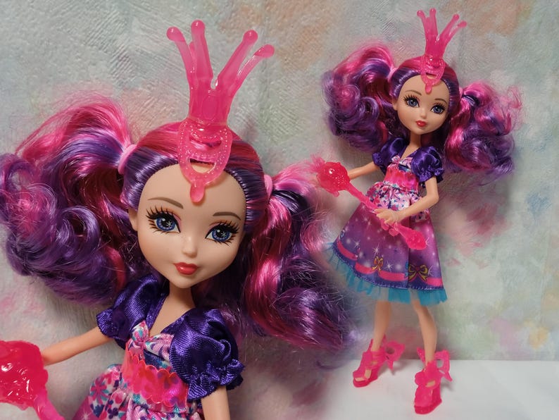 K&ouml;nnte beinhalten: Zwei Modepuppen mit pinken und lila Haaren, die lila und rosa Kleider und pinkfarbene Accessoires tragen. Die Puppen haben blaue Augen und posieren vor einem hellen Hintergrund. Eine Puppe ist im Vordergrund, die andere im Hintergrund.