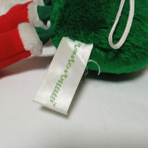 K&ouml;nnte beinhalten: Gr&uuml;ner Pl&uuml;sch-Weihnachtsbaumschmuck mit roten und wei&szlig;en Filzstiefeln und einem wei&szlig;en Etikett mit der Aufschrift "Love-a-Letters TM".