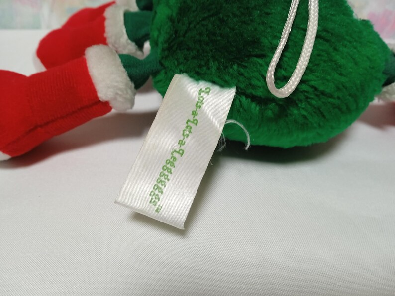 K&ouml;nnte beinhalten: Gr&uuml;ner Pl&uuml;sch-Weihnachtsbaumschmuck mit roten und wei&szlig;en Filzstiefeln und einem wei&szlig;en Etikett mit der Aufschrift "Love-a-Letters TM".