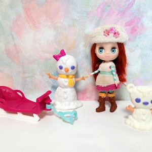 May include: A collection of winter-themed toys, including a doll with red hair and a white hat, a snowman with a pink bow, a pink sled, and a white bear figurine. The doll is wearing a dress and boots. The toys are set against a colorful background.