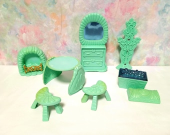 Op de afbeelding: Een set teal-kleurige plastic poppenhuis meubels, waaronder een kaptafel met een spiegel, een tafel, twee stoelen, een open haard, een kist en een kapstok.