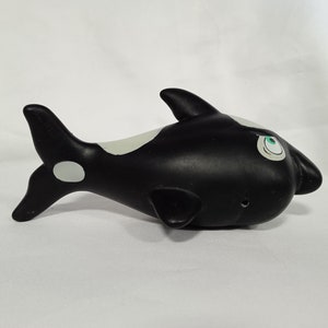 K&ouml;nnte beinhalten: Schwarz-wei&szlig;es Orca-Spielzeug aus Gummi mit gr&uuml;nen Augen. Die Orca hat einen wei&szlig;en Fleck auf ihrer Schwanzflosse.