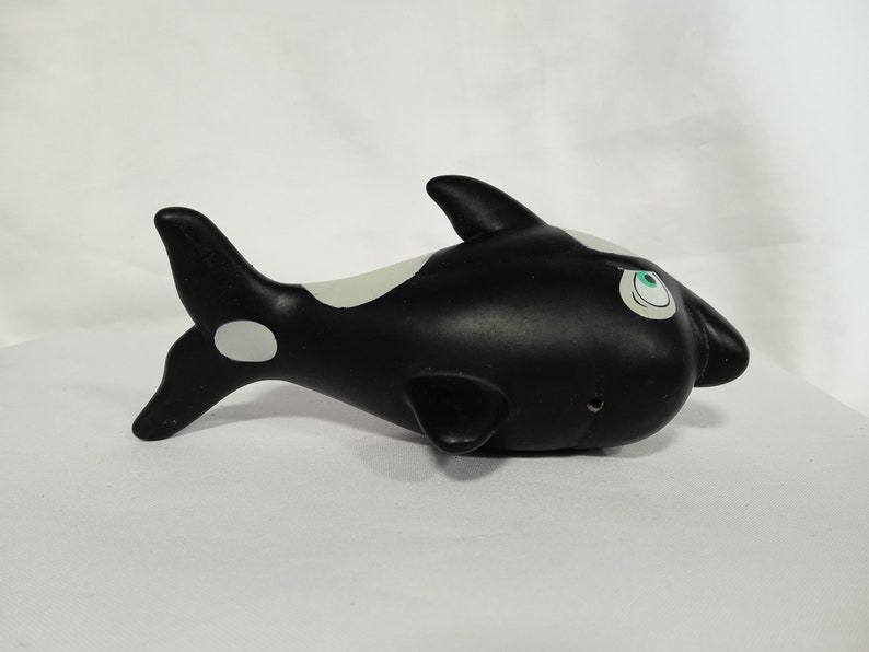 K&ouml;nnte beinhalten: Schwarz-wei&szlig;es Orca-Spielzeug aus Gummi mit gr&uuml;nen Augen. Die Orca hat einen wei&szlig;en Fleck auf ihrer Schwanzflosse.