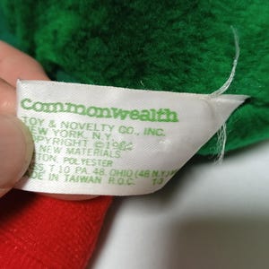 K&ouml;nnte beinhalten: Ein wei&szlig;es Etikett mit gr&uuml;nem Text, der "Commonwealth Toy & Novelty Co., Inc. New York, N.Y. Copyright &copy;19 New Materials 100% Polyester Made in Taiwan R.O.C. 73" lautet.
