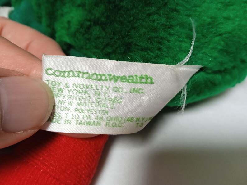K&ouml;nnte beinhalten: Ein wei&szlig;es Etikett mit gr&uuml;nem Text, der "Commonwealth Toy & Novelty Co., Inc. New York, N.Y. Copyright &copy;19 New Materials 100% Polyester Made in Taiwan R.O.C. 73" lautet.