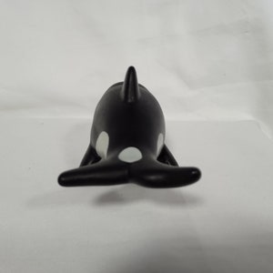 K&ouml;nnte beinhalten: Schwarze und wei&szlig;e Plastikfigur eines Orca-Wals. Der Orca ist mit dem R&uuml;cken zur Kamera gerichtet, seine R&uuml;ckenflosse und sein Schwanz sind sichtbar.