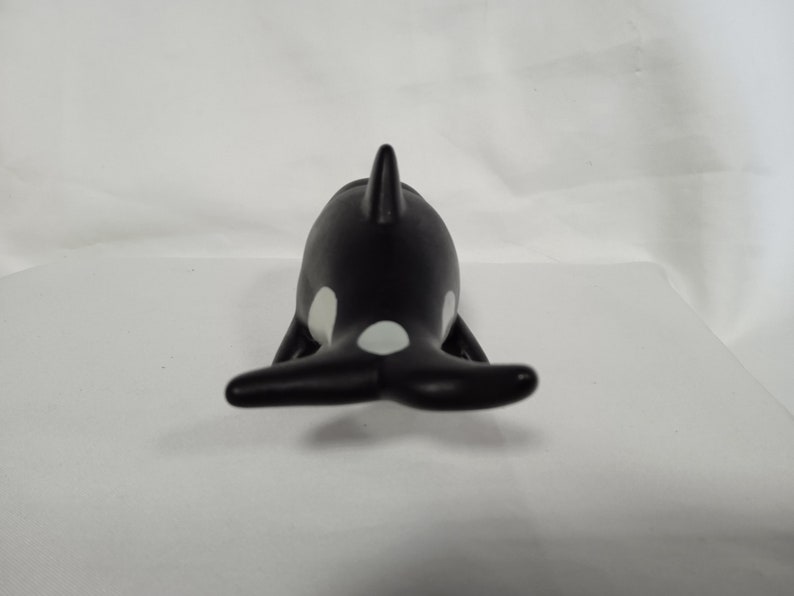 K&ouml;nnte beinhalten: Schwarze und wei&szlig;e Plastikfigur eines Orca-Wals. Der Orca ist mit dem R&uuml;cken zur Kamera gerichtet, seine R&uuml;ckenflosse und sein Schwanz sind sichtbar.