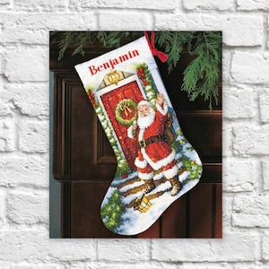 Puede incluir: Una media de Navidad roja y blanca con una ilustración de Papá Noel. La media está personalizada con el nombre "Benjamin" bordado.