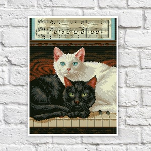 May include: A black cat and a white cat sitting on a piano keyboard. The cats are looking at the camera. The piano has sheet music on top of it.
