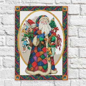 May include: A colorful cross-stitch pattern of Santa Claus holding a teddy bear and a bag of toys. He is wearing a red and green suit with a white beard and a red hat. The background is a white oval with a gold frame.