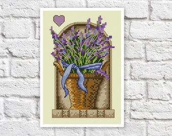 May include: A cross-stitch pattern of a lavender bouquet in a brown pot with a blue ribbon, set in a decorative frame with a heart above it.