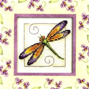 Peut inclure: Un motif de point de croix représentant une libellule colorée aux ailes orange, jaunes et violettes sur un fond blanc. La libellule est entourée d'une bordure violette et d'un motif floral de feuilles vertes et de fleurs violettes.