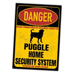 Op de afbeelding: Een geel en zwart waarschuwingsbord met de tekst "DANGER" in een rode ovaal. Het bord luidt "DIESES GRUNDSTÜCK IST GESCHÜTZT DURCH EIN PUGGLE HOME SECURITY SYSTEM BETRETEN AUF EIGENE GEFAHR!" en toont een silhouet van een puggle-hond.