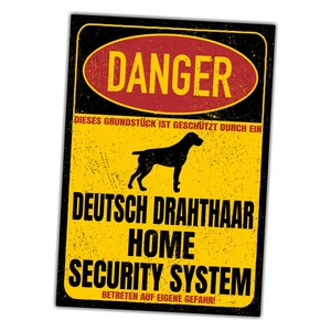 Könnte beinhalten: Ein gelbes und schwarzes Warnschild mit dem Text "DANGER" in einem roten Kreis. Das Schild lautet "DIESES GRUNDSTÜCK IST GESCHÜTZT DURCH EIN DEUTSCH DRAHTHAAR HOME SECURITY SYSTEM BETRETEN AUF EIGENE GEFAHR!" und zeigt die Silhouette eines Deutsch Drahthaar.
