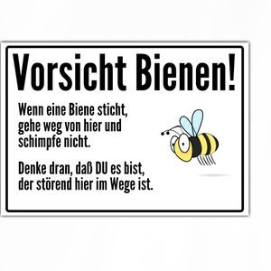 Op de afbeelding: Een wit bord met zwarte tekst die "Vorsicht Bienen!" zegt. Het bord bevat ook een cartoon-bij en tekst die zegt "Wenn eine Biene sticht, gehe weg von hier und schimpfe nicht. Denke dran, daß DU es bist, der störend hier im Wege ist."