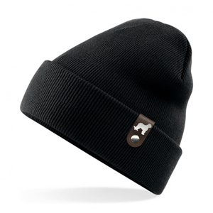 Könnte beinhalten: Schwarze Mütze mit einem braunen Leder-Patch, der eine weiße Silhouette eines Hundes zeigt.