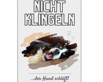 Könnte beinhalten: Ein weißes Schild mit schwarzem Text, auf dem "NICHT KLINGELN...der Hund schläft!" steht. Ein brauner und weißer Hund schläft auf einem braunen Sofa. Der Hund gähnt mit offenem Maul. Das Schild ist eine humorvolle Erinnerung, nicht an der Tür zu klingeln, weil der Hund schläft.