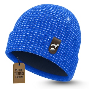 Könnte beinhalten: Eine leuchtend blaue Mütze mit einem strukturierten Strickmuster und einem braunen Lederetikett mit einer Dackelsilhouette. Die Mütze hat einen umgeschlagenen Saum und ein kleines Etikett mit Text. Ein Winteraccessoire.
