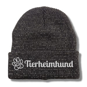 Könnte beinhalten: Schwarz-weiße Strickmütze mit einem weißen Pfotenabdruck und dem Text "Tierheimhund" am Bündchen.