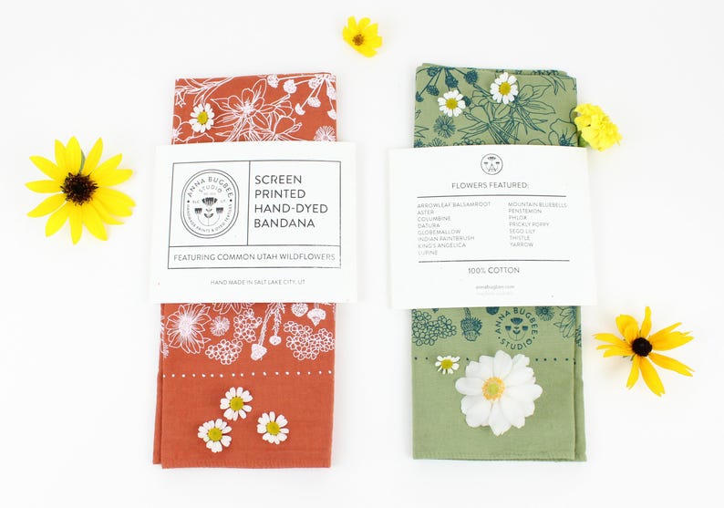 Peut inclure: Deux bandanas en coton teints &agrave; la main avec des illustrations de fleurs sauvages de l'Utah imprim&eacute;es &agrave; l'&eacute;cran. Le bandana de gauche est orange avec des fleurs blanches. Le bandana de droite est vert avec des fleurs blanches. Les bandanas sont 100% coton et faits &agrave; la main &agrave; Salt Lake City, Utah.