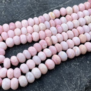 Puede incluir: Una hebra de cuentas de ópalo rosa con forma redondeada y facetada. Las cuentas están enhebradas en un hilo transparente y tienen un aspecto natural y orgánico.