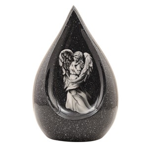 May include: Black teardrop-shaped ceramic urn with a white angel design. The urn has a speckled finish.