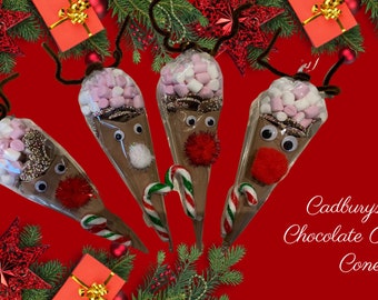 May include: Four Cadbury's Hot Chocolate Reindeer Cones decorated with marshmallows, candy canes, and googly eyes. The cones are on a red background with Christmas decorations.