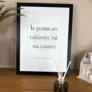 May include: A framed print with a green Celtic knot design and the Irish Gaelic phrase "Is fearr an tsláinte ná na cáinte" which translates to "Health is better than wealth".