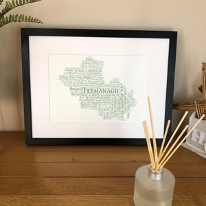 May include: A framed print of a word cloud art piece in the shape of Northern Ireland. The word cloud is made up of words and phrases related to the county of Fermanagh, including "Banjaxed", "Bloctered", "Not a bout to doubt it", and "Hang sangwich".