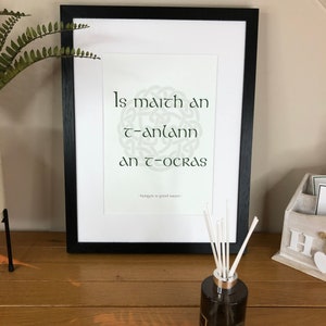 May include: A framed print with a Celtic knot design and the Irish phrase "Is maith an t-anlann an t-ocras" which translates to "Hunger is a good sauce".