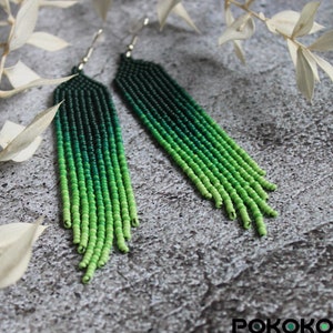 May include: A pair of long, green beaded earrings with a gradient from dark green to light green. The earrings are hanging from silver hooks.