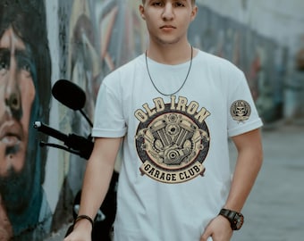 May include: White t-shirt with a circular graphic featuring a motorcycle engine and the text "OLD IRON GARAGE CLUB." A smaller skull emblem is on the right sleeve. The person is wearing a black watch and bracelet.