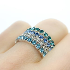 May include: A silver ring with a multi-colored ombre design. The ring is set with blue and green rhinestones.
