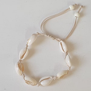 May include: A white shell bracelet with a knotted cord and white bead accents.