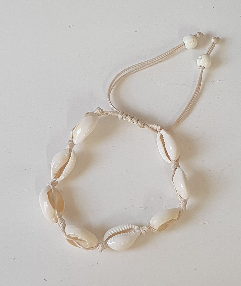 May include: A white shell bracelet with a knotted cord and white bead accents.