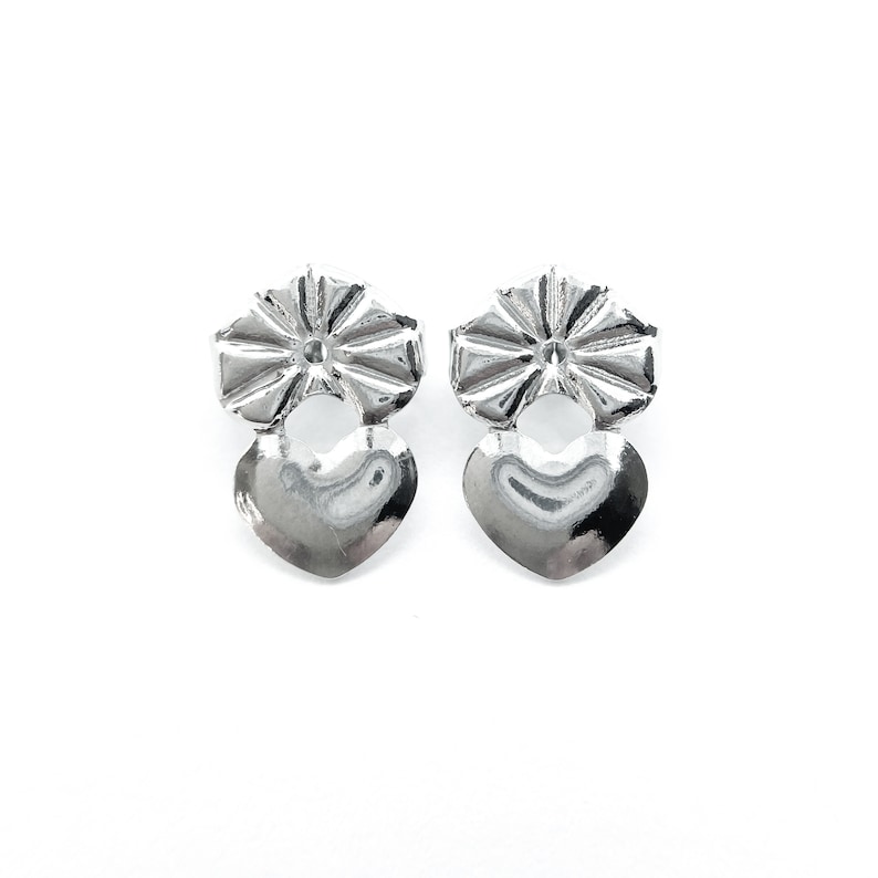 Pode incluir: Um par de brincos de prata com um charme em forma de cora&ccedil;&atilde;o e um charme decorativo em forma de flor.