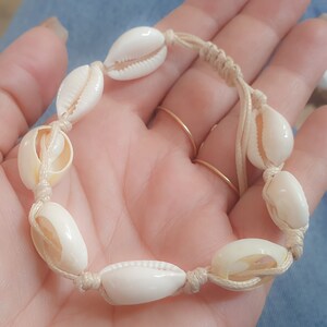 May include: A white shell bracelet with a beige cord. The bracelet is made of natural seashells and is tied with a simple knot.