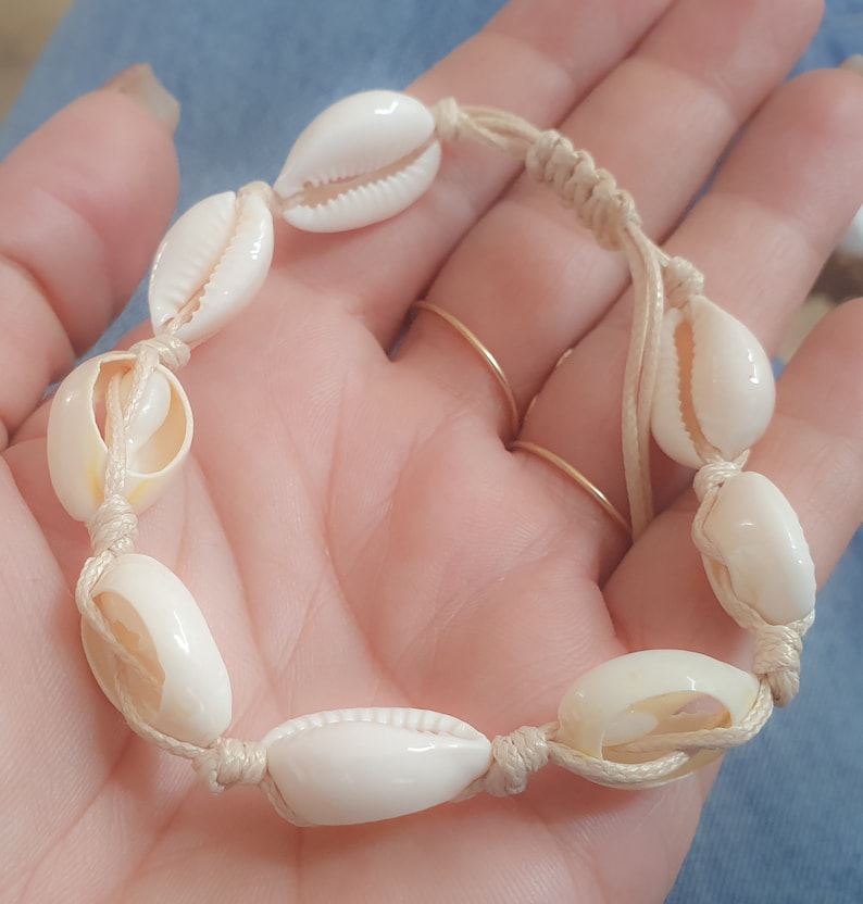 May include: A white shell bracelet with a beige cord. The bracelet is made of natural seashells and is tied with a simple knot.