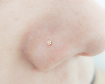 Op de afbeelding: Een close-up van iemands neus met een kleine, heldere edelsteen neusring.