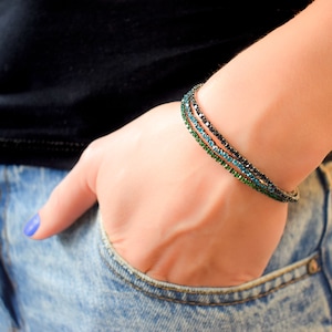 Puede incluir: Tres pulseras superpuestas con detalles de cristal negro, azul y verde.
