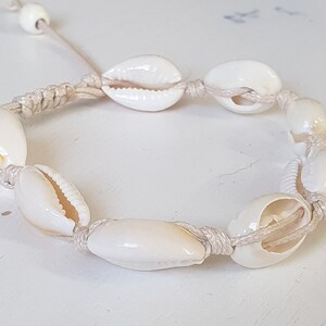 May include: A white shell bracelet with a natural rope cord. The bracelet is made with cowrie shells and has a simple design.