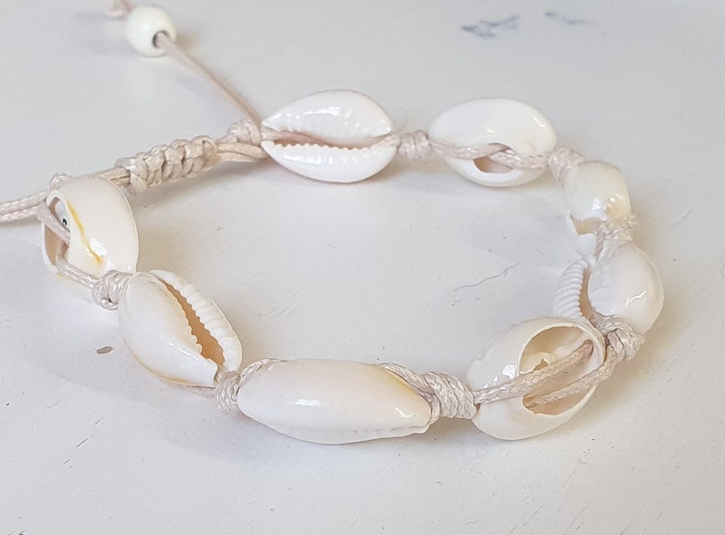 May include: A white shell bracelet with a natural rope cord. The bracelet is made with cowrie shells and has a simple design.