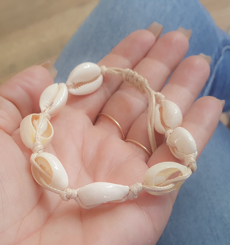 May include: A white shell bracelet with a beige cord. The bracelet is made of natural seashells and is tied with a simple knot.