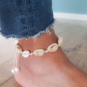 May include: A white seashell anklet with a white string and white beads. The anklet is on a person's ankle.